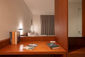 Ett hotellrum med ett skrivbord i trä, böcker, en lampa, ett fönster med gardiner och en dörr.