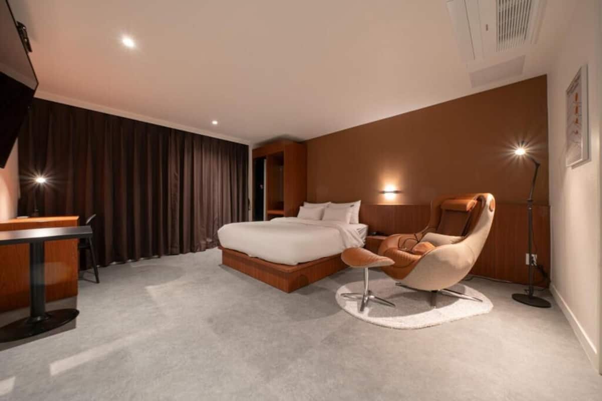 Ett modernt hotellrum med en säng, ett skrivbord, en stol och en golvlampa.