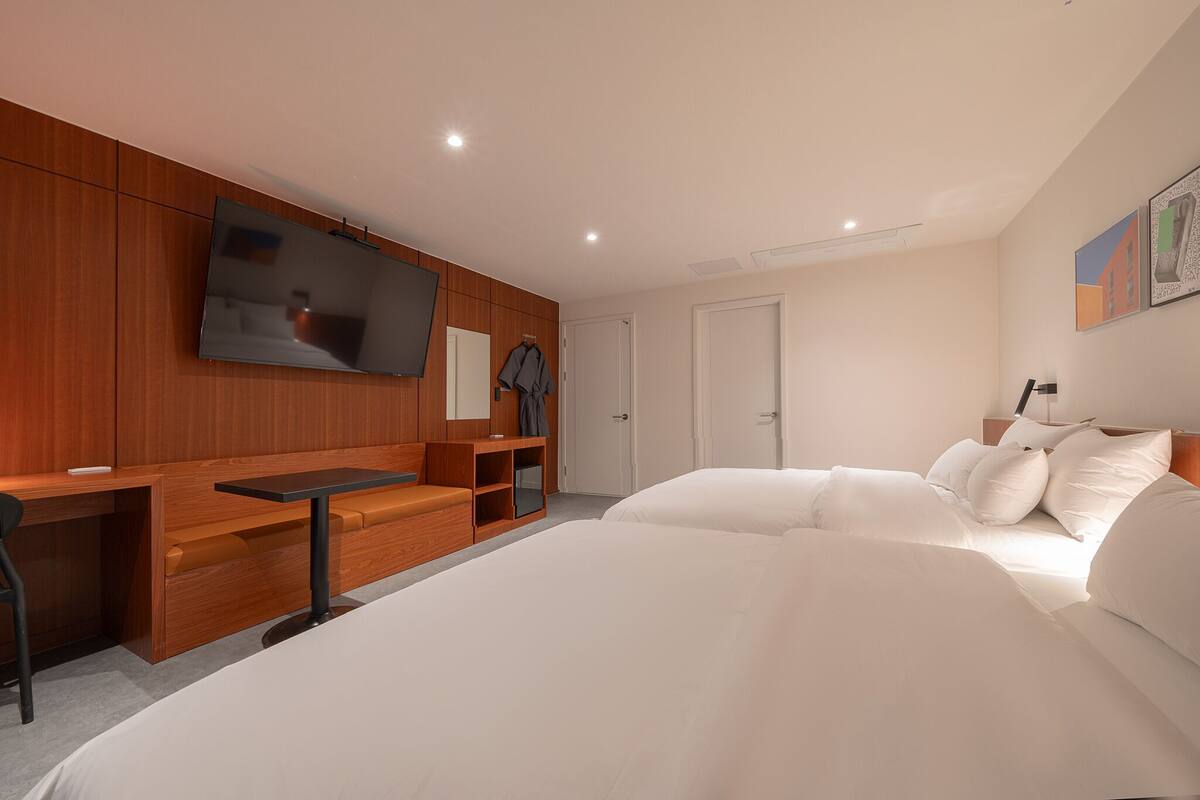 Ett modernt hotellrum med en platt-TV, ett skrivbord i trä, en soffa, en säng med vita sängkläder och en tavla på väggen.