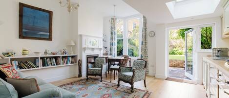 A bright living room with a sofa, a patterned rug, and a dining area with chairs and a table.
