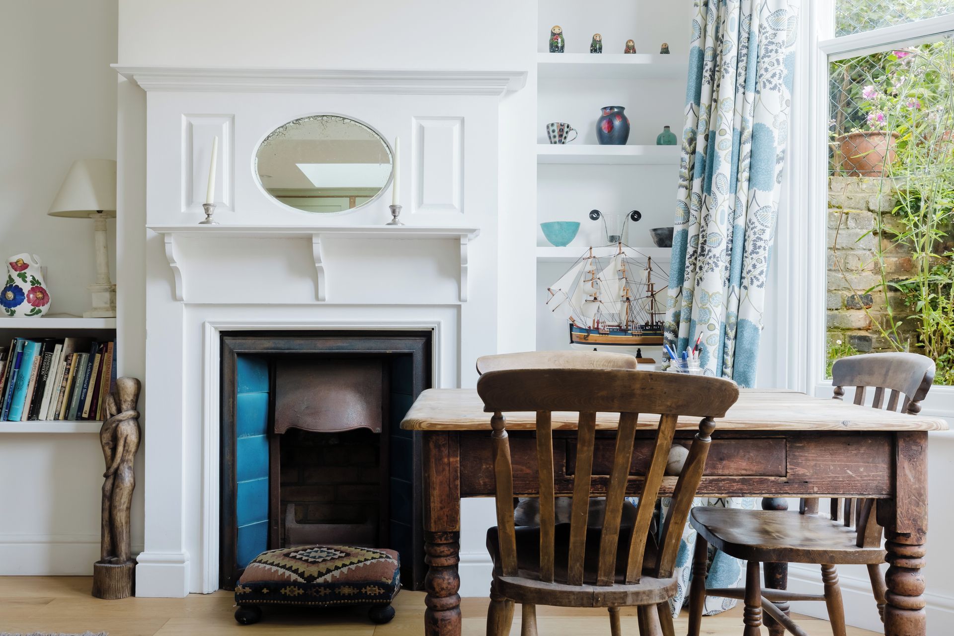 A room with a fireplace, wooden furniture, and a view of greenery outside.