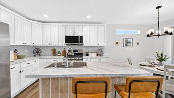 A modern kitchen with white cabinets, a stainless steel sink, and a marble island with two chairs.