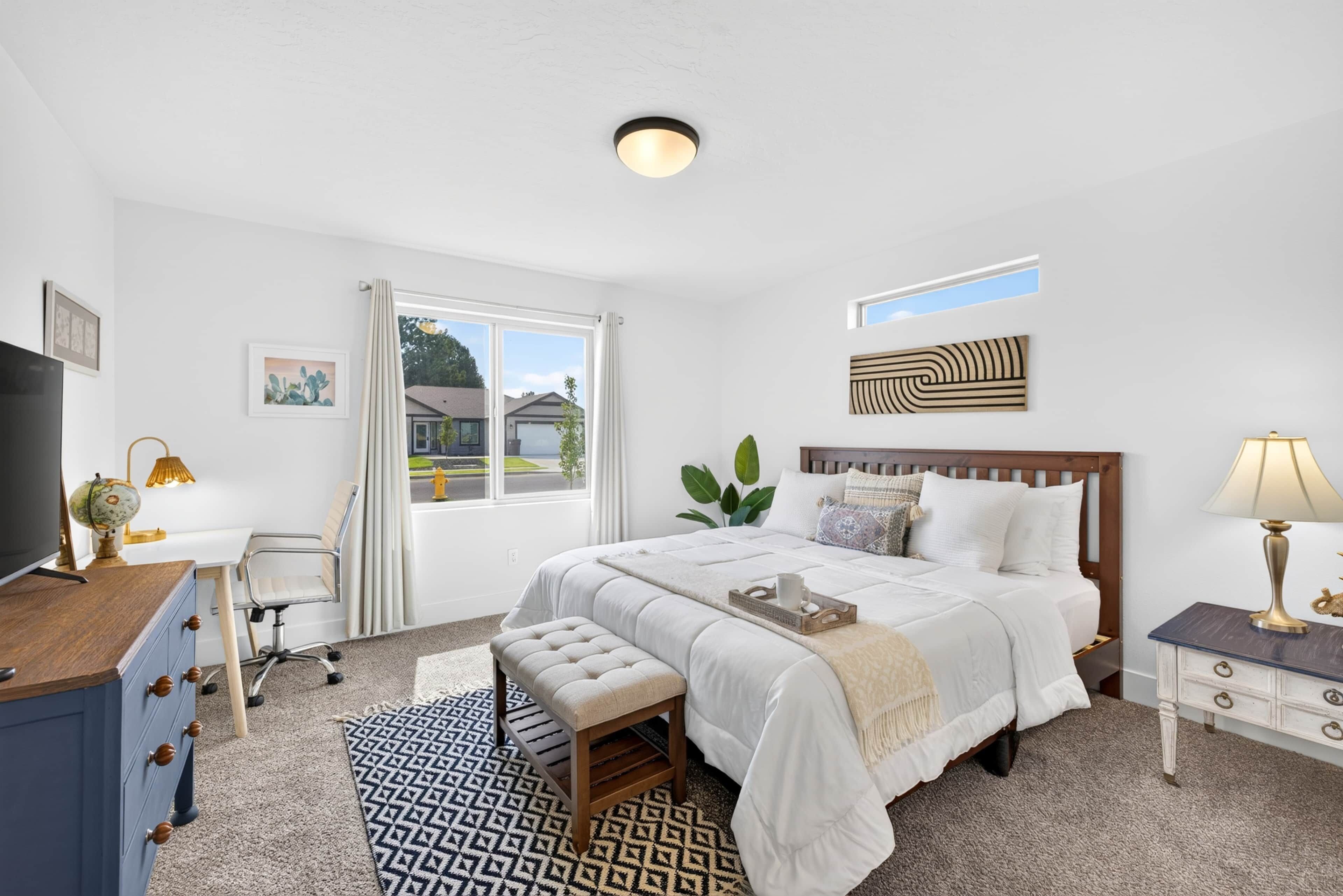 A bedroom with a large bed, a desk with a globe, a chair, a dresser, a window with a view, and a ceiling light.