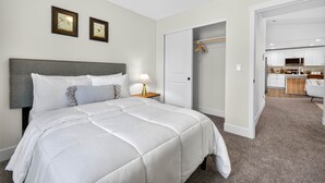 Ein Hotelzimmer mit einem Bett, einem Nachttisch, einer Lampe, einem Schrank und Blick zur Küche.