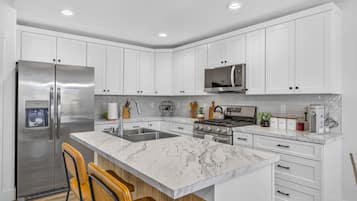 Una cocina moderna con armarios blancos, electrodomésticos de acero inoxidable, una isla de mármol y un horno empotrado.