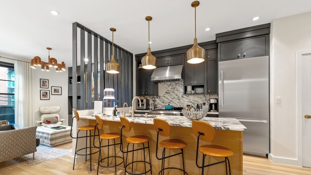 Une cuisine moderne dotée d’un îlot en marbre, de tabourets de bar, de luminaires suspendus et d’un réfrigérateur en acier inoxydable.