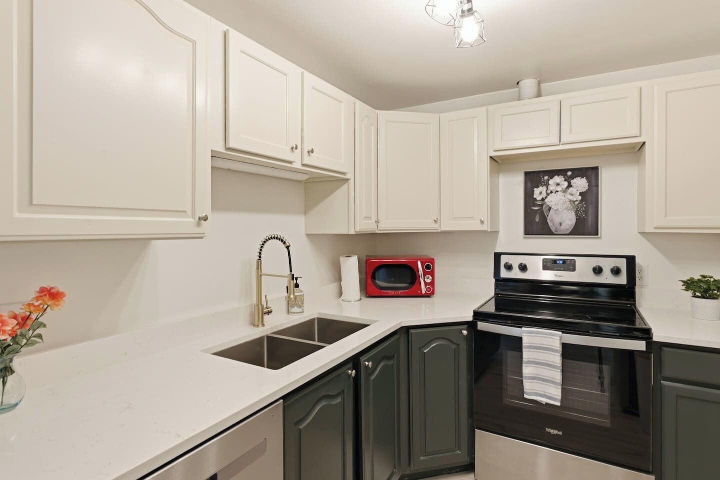 A kitchen with white cabinets, a red microwave, a black stove, and a vase with flowers on the counter.