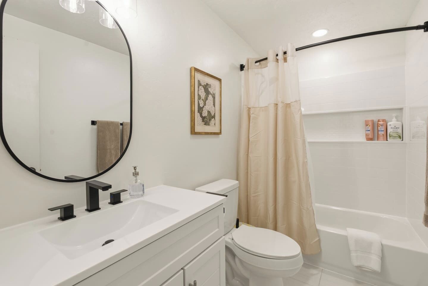 A bathroom with a round mirror, two sinks, a toilet, a bathtub, and a shower curtain.