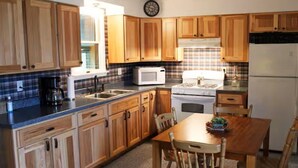 A kitchen with wooden cabinets, a microwave, stove, refrigerator, and a dining table with chairs. - Copper Roof Getaway Golconda, Il (Golconda)