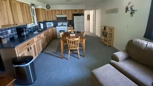 A compact kitchen with wooden cabinets, a dining table with chairs, a sofa, and a trash bin. - Copper Roof Getaway Golconda, Il (Golconda)