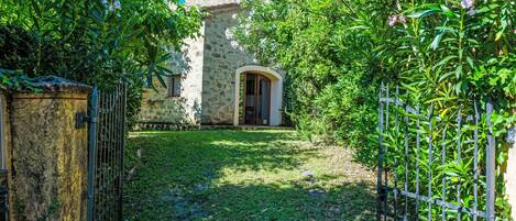 A stone building with a garden entrance, a metal gate, and a paved path leading to the door.