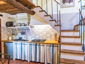 A kitchen with a gas stove, a refrigerator, and a microwave. There is a staircase with wooden steps and blue railings. - Fibbialla by Interhome (Pescia)