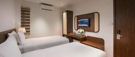 A hotel room with two beds, a desk, a TV mounted on the wall, and a door.