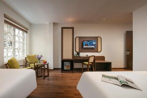 A hotel room with two beds, a desk with a computer, a TV mounted on the wall, and a window with a view of the city. - Pavilion Essence Hanoi Hotel (Hanoi)