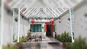 Ein überdachter Patio-Bereich mit Tisch und Stühlen, Topfpflanzen und einer Tür mit roten Verzierungen.