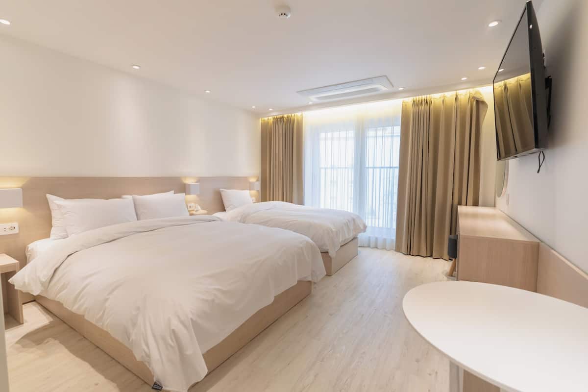 Une chambre d’hôtel avec deux lits, une table de chevet, un téléviseur fixé au mur et une grande fenêtre avec des rideaux.