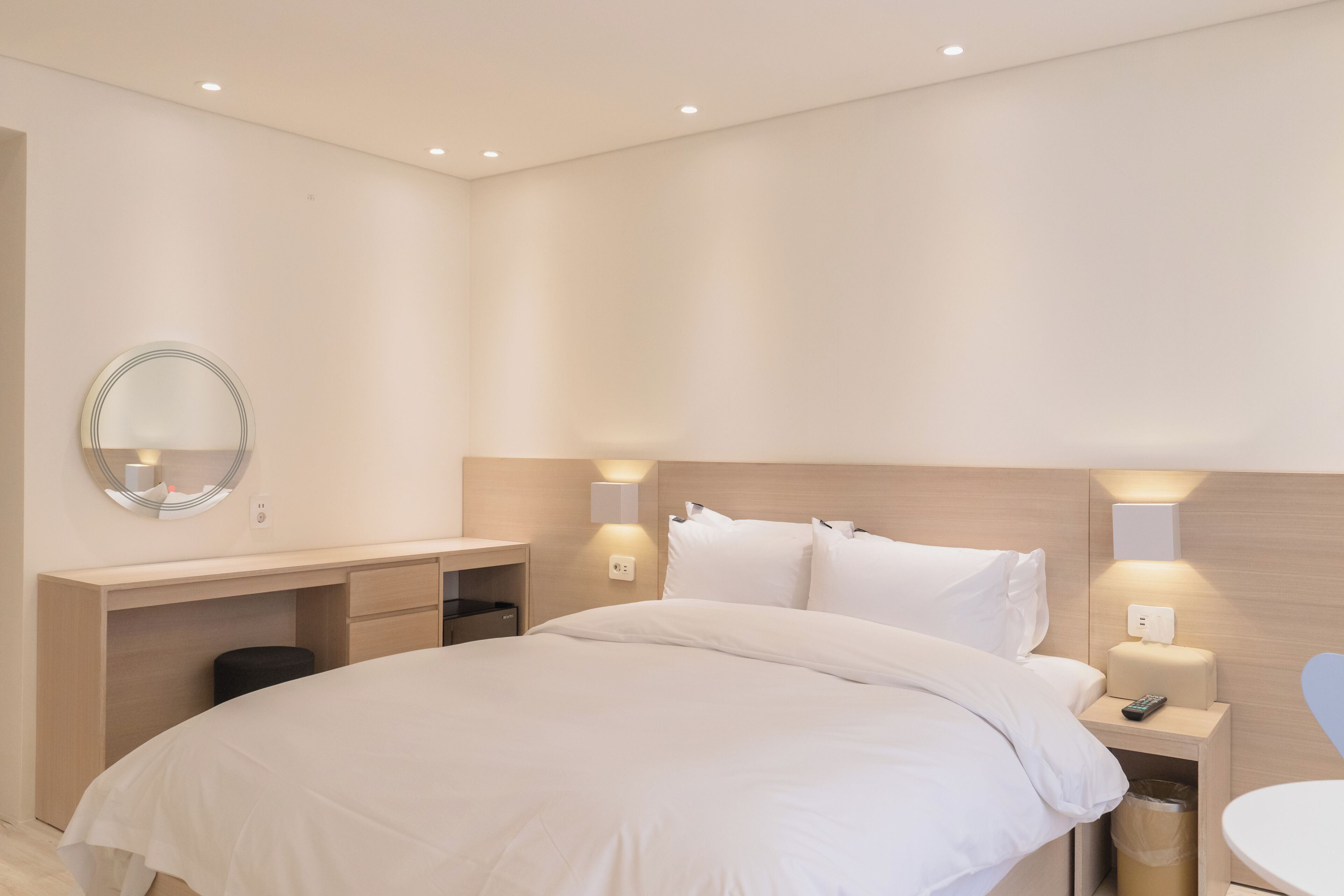 A modern hotel room with a large bed, a desk, a mirror, and bedside lamps.