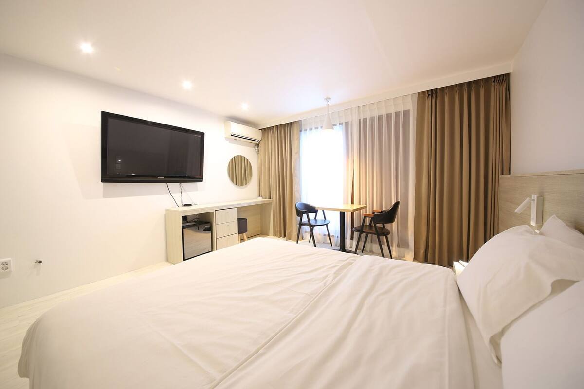 Une chambre d’hôtel comprenant un lit, un bureau avec une chaise, une télévision et une fenêtre avec des rideaux.