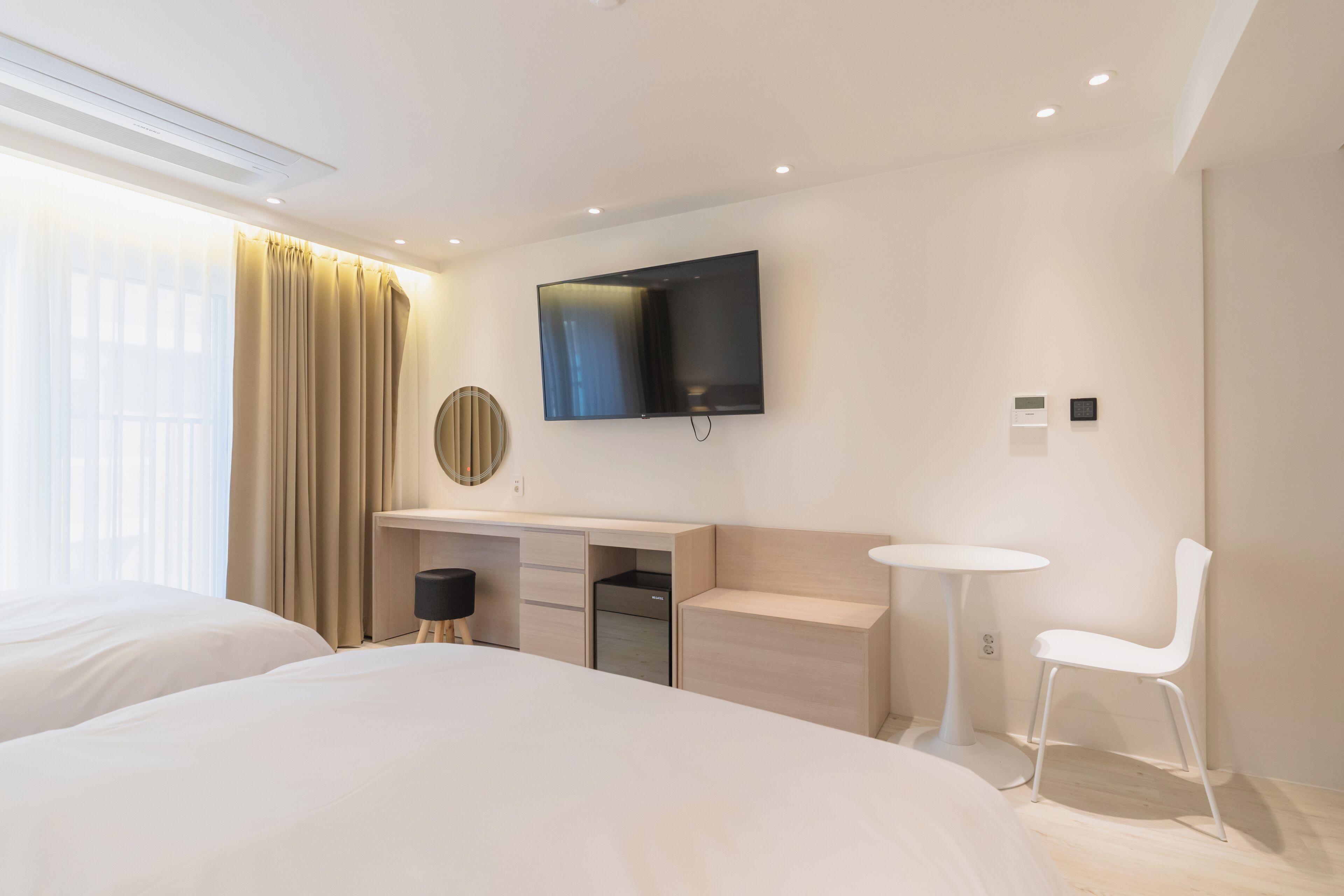 Ein modernes Hotelzimmer mit einem Bett, einem Schreibtisch, einem Sessel, einem Fernseher und einem Fenster mit Vorhängen.