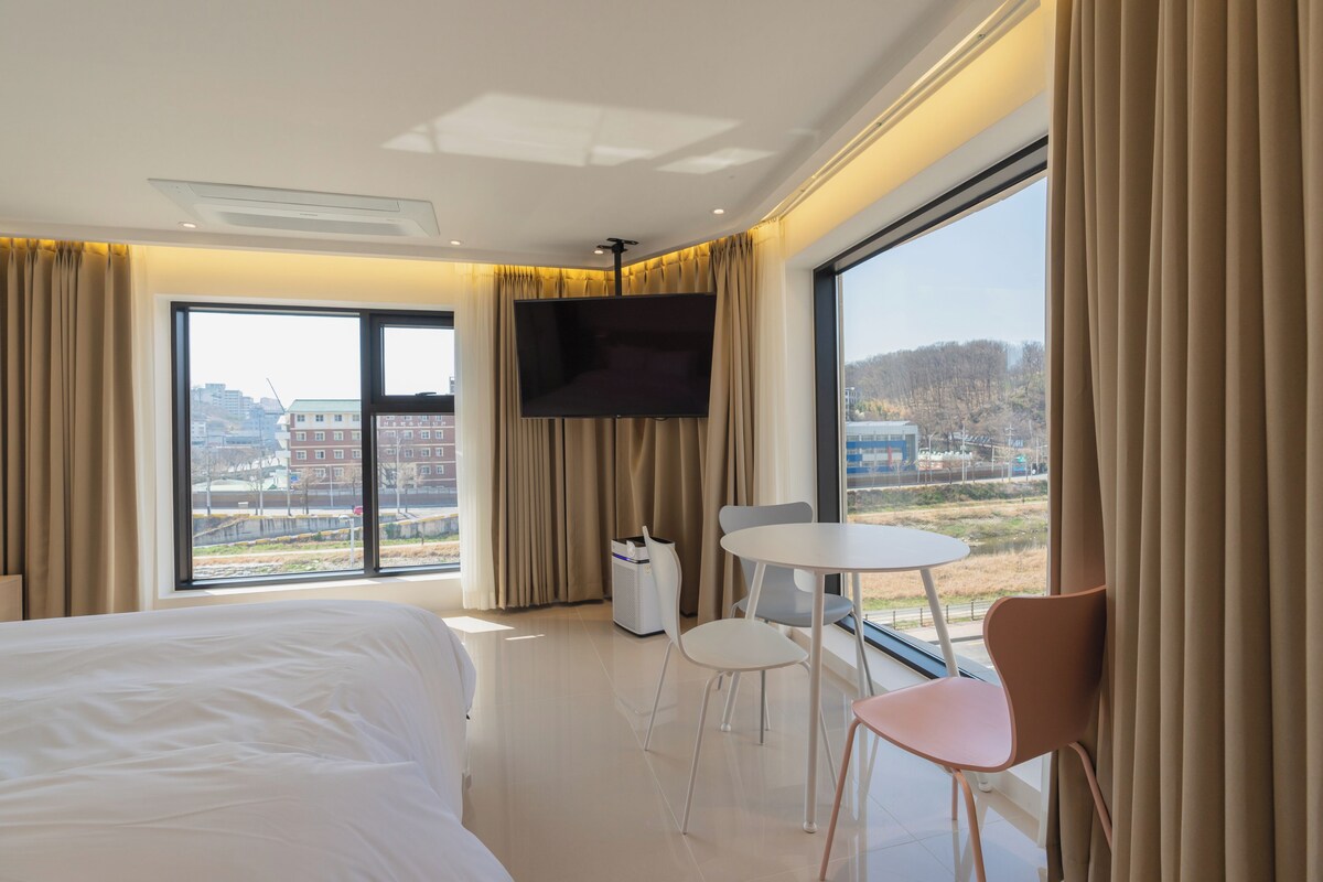 Une chambre d’hôtel avec un lit, une télévision, une petite table avec deux chaises et une grande fenêtre avec des rideaux.