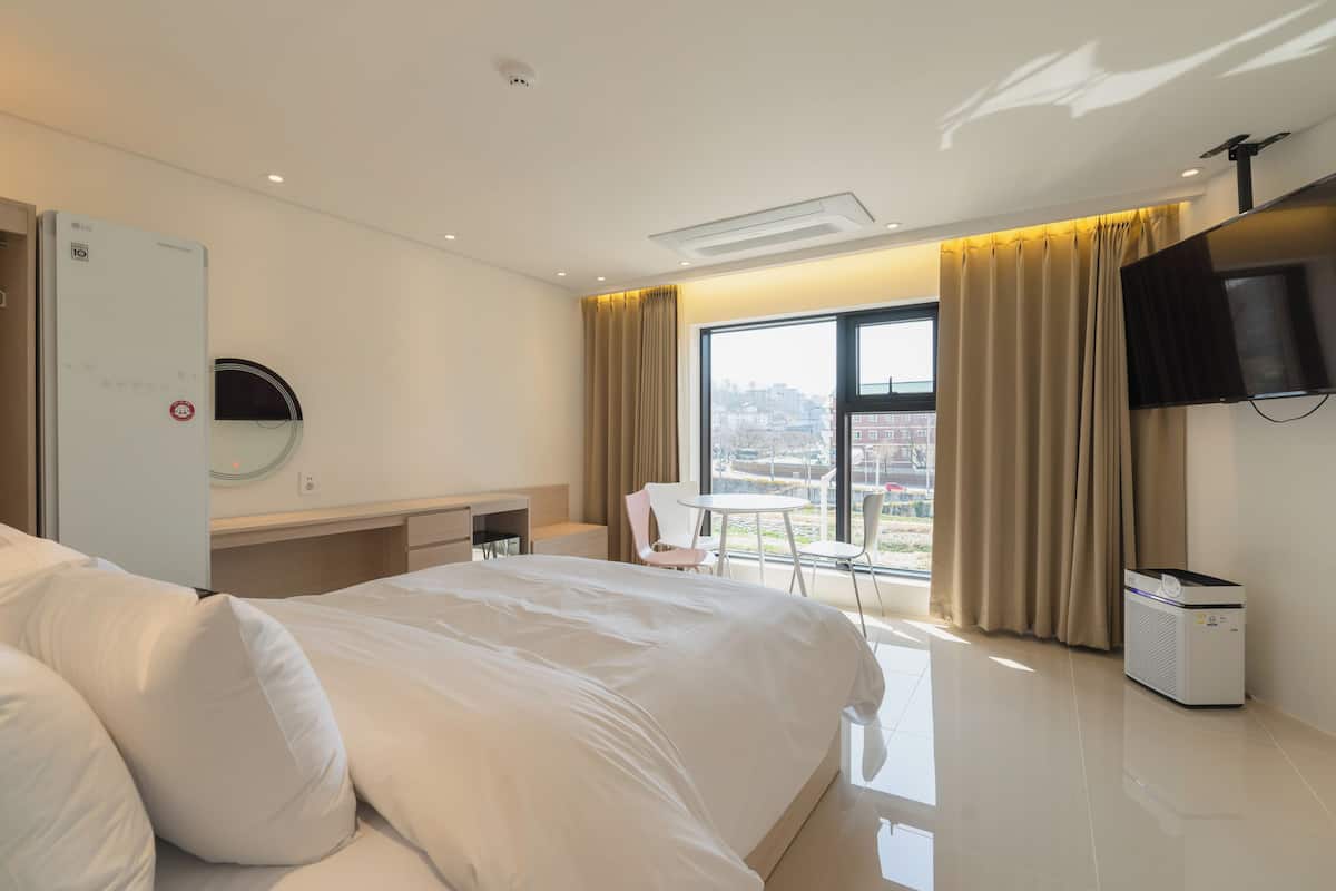 Une chambre d’hôtel avec un lit, un bureau, une chaise, une télévision et une fenêtre donnant sur un paysage agréable.