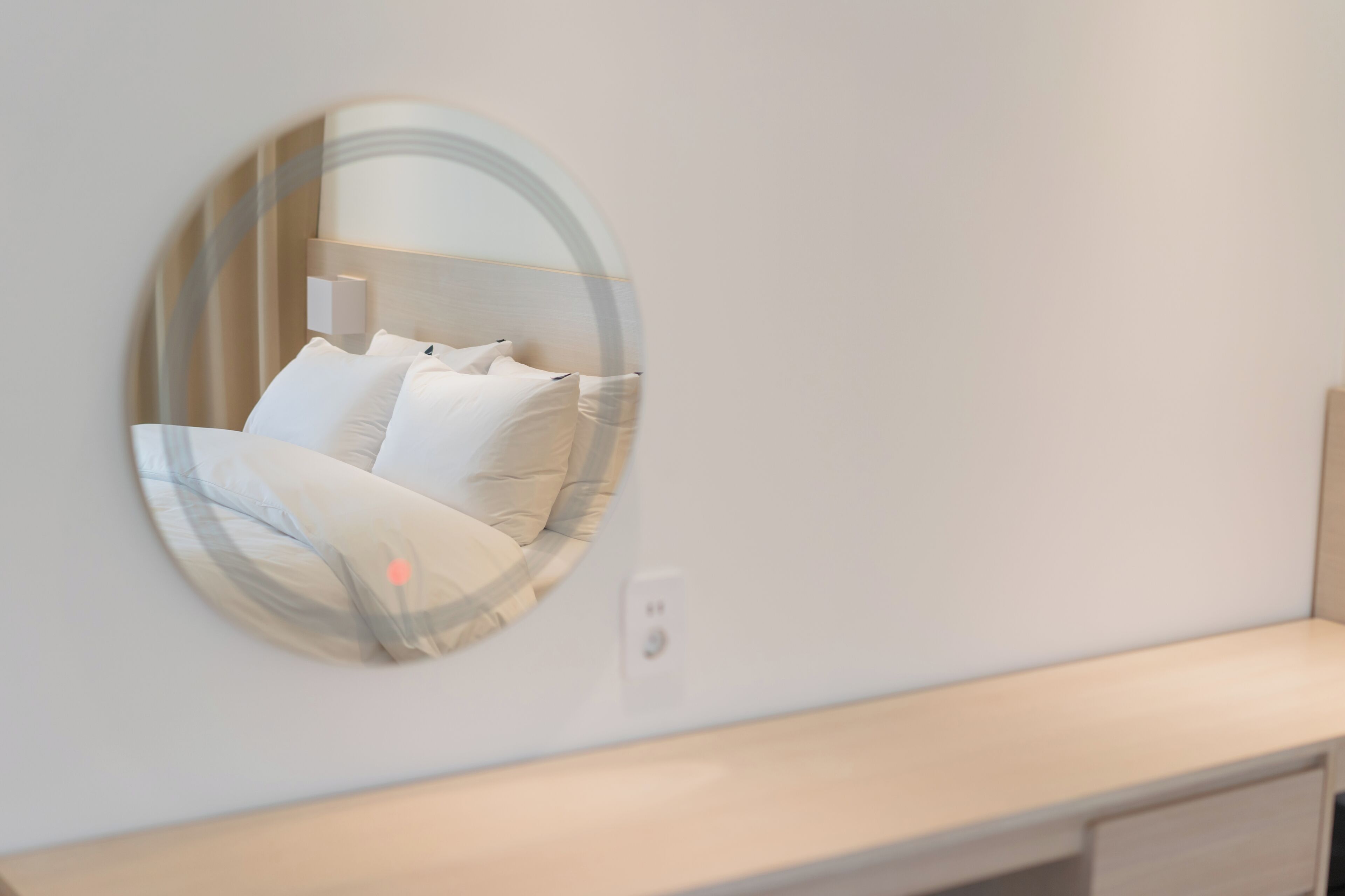 Un espejo redondo refleja una cama con ropa blanca y una mesita de noche.