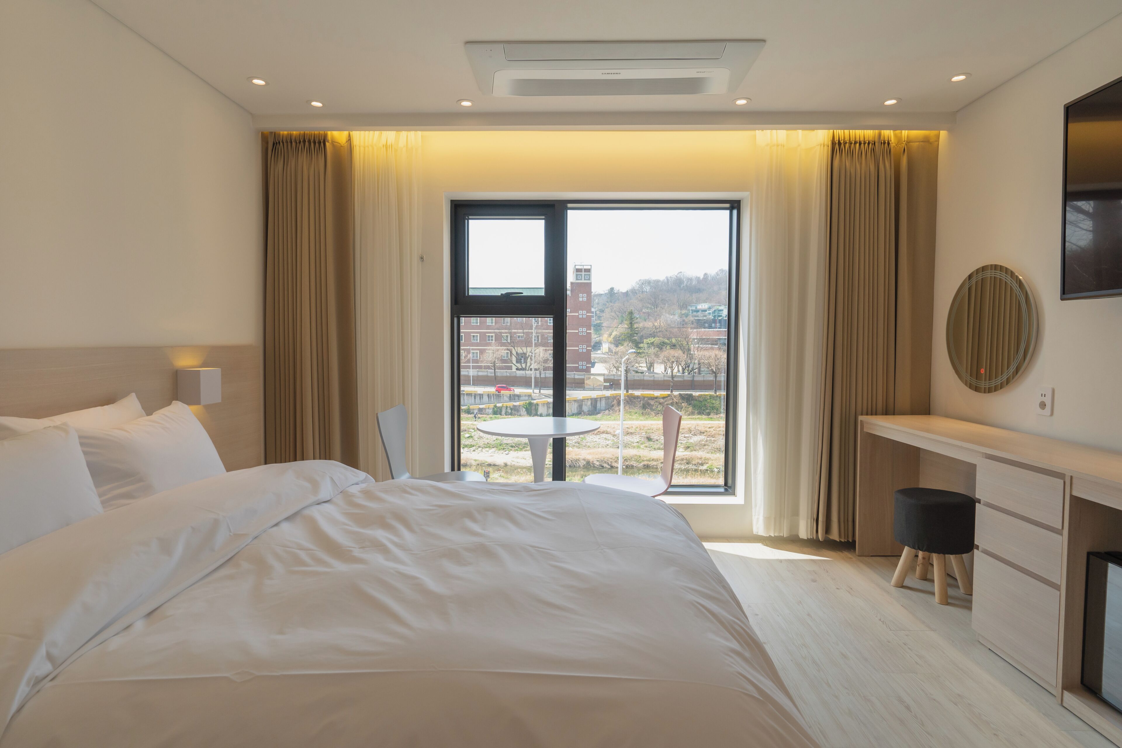 Habitación de hotel con una cama grande, un escritorio, una silla y vistas a la ciudad a través de la ventana.