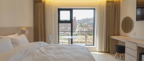 Habitación de hotel con una cama grande, un escritorio, una silla y vistas a la ciudad a través de la ventana.