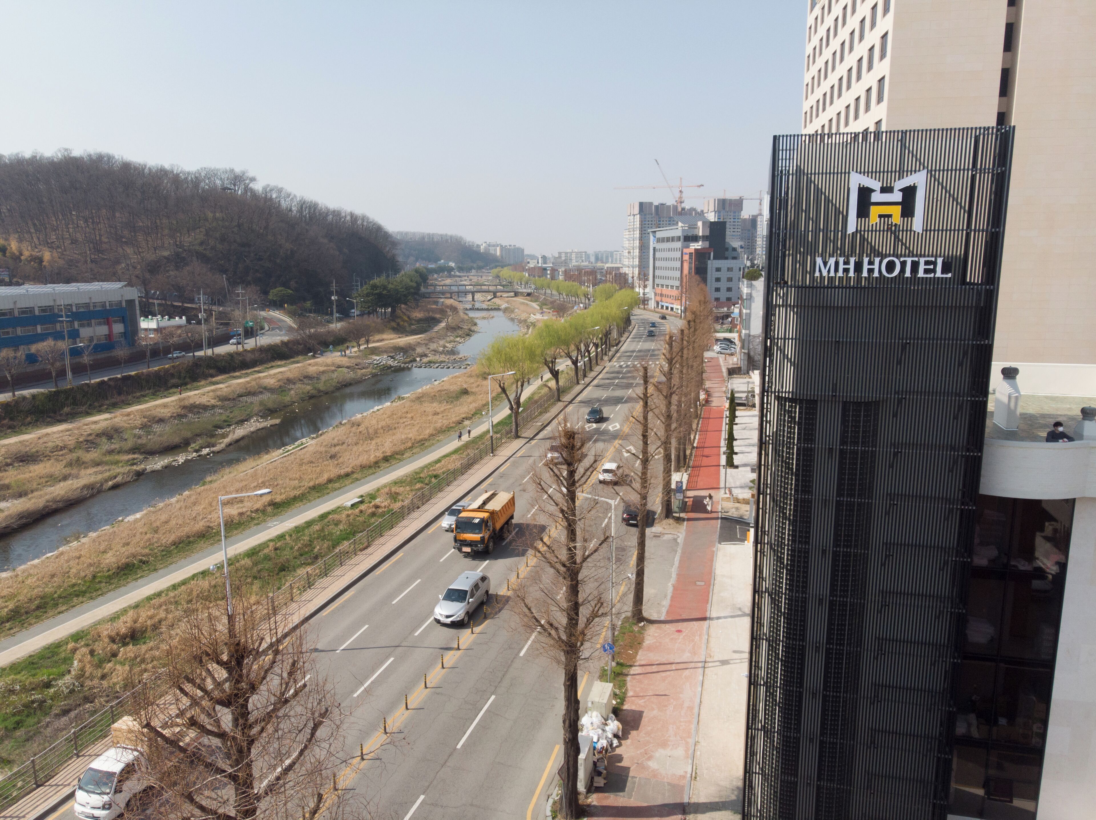 A modern hotel with a prominent logo, a river running parallel to the road, and a clear view of the surrounding urban landscape.