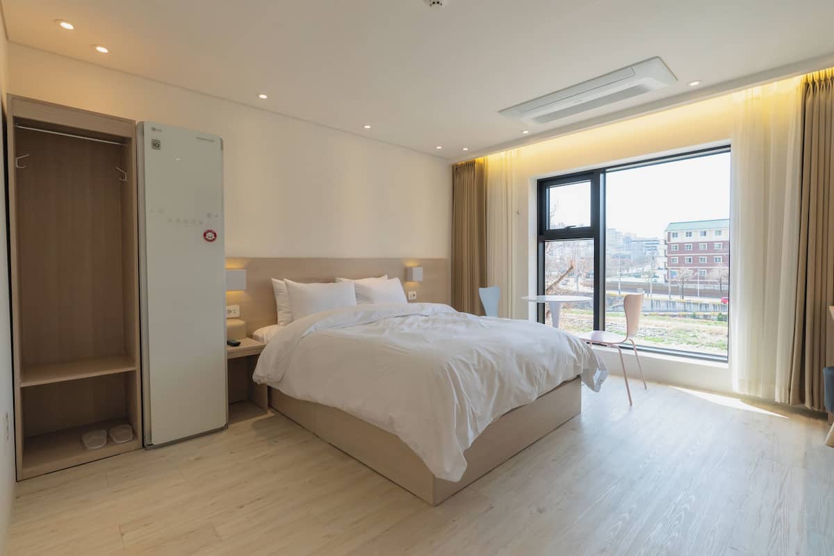Une chambre d’hôtel moderne, équipée d’un lit, d’une table de chevet, d’une lampe et offrant une vue sur la ville grâce à une grande fenêtre.