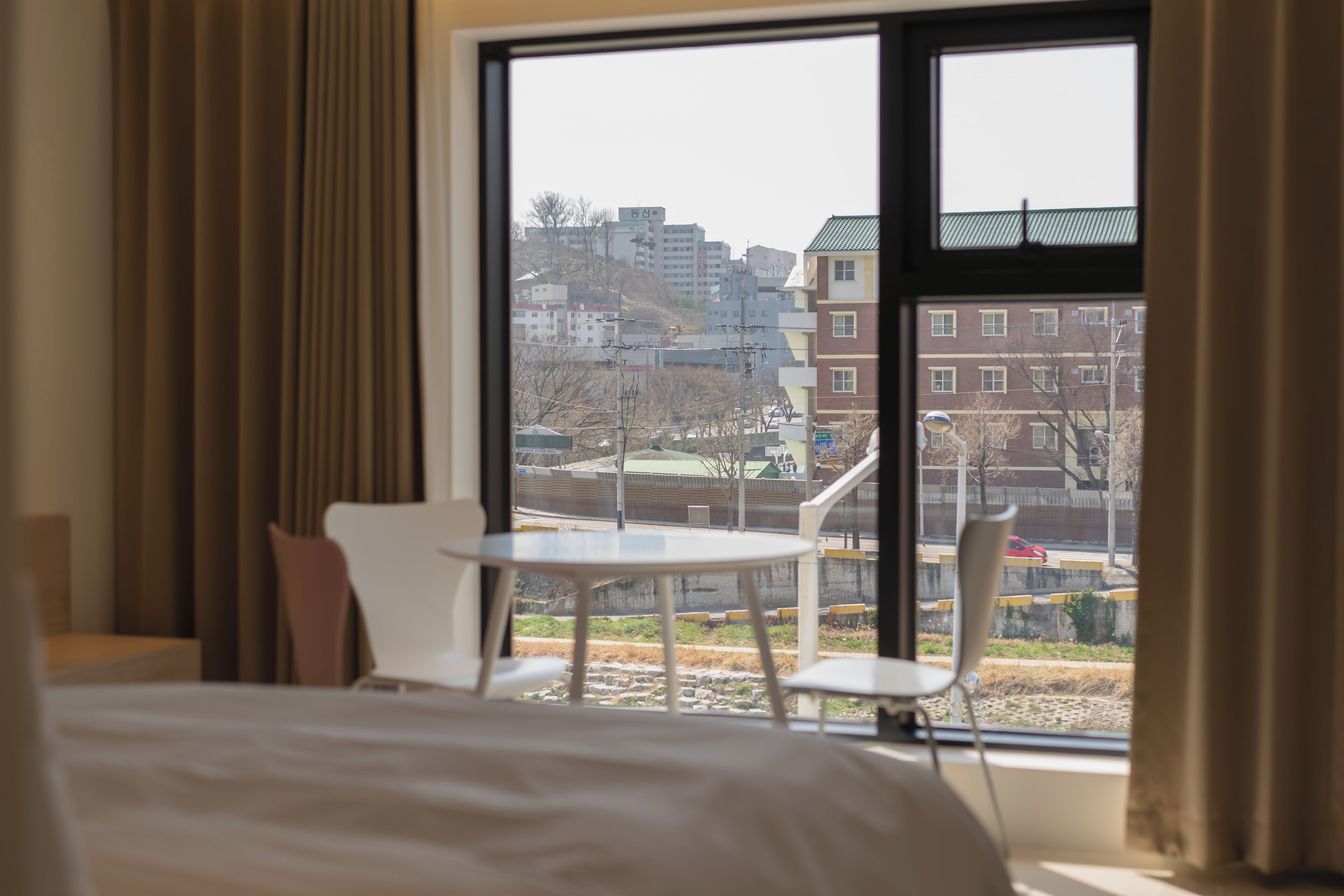 A hotel room with a large window, a bed, a small table, and two chairs.