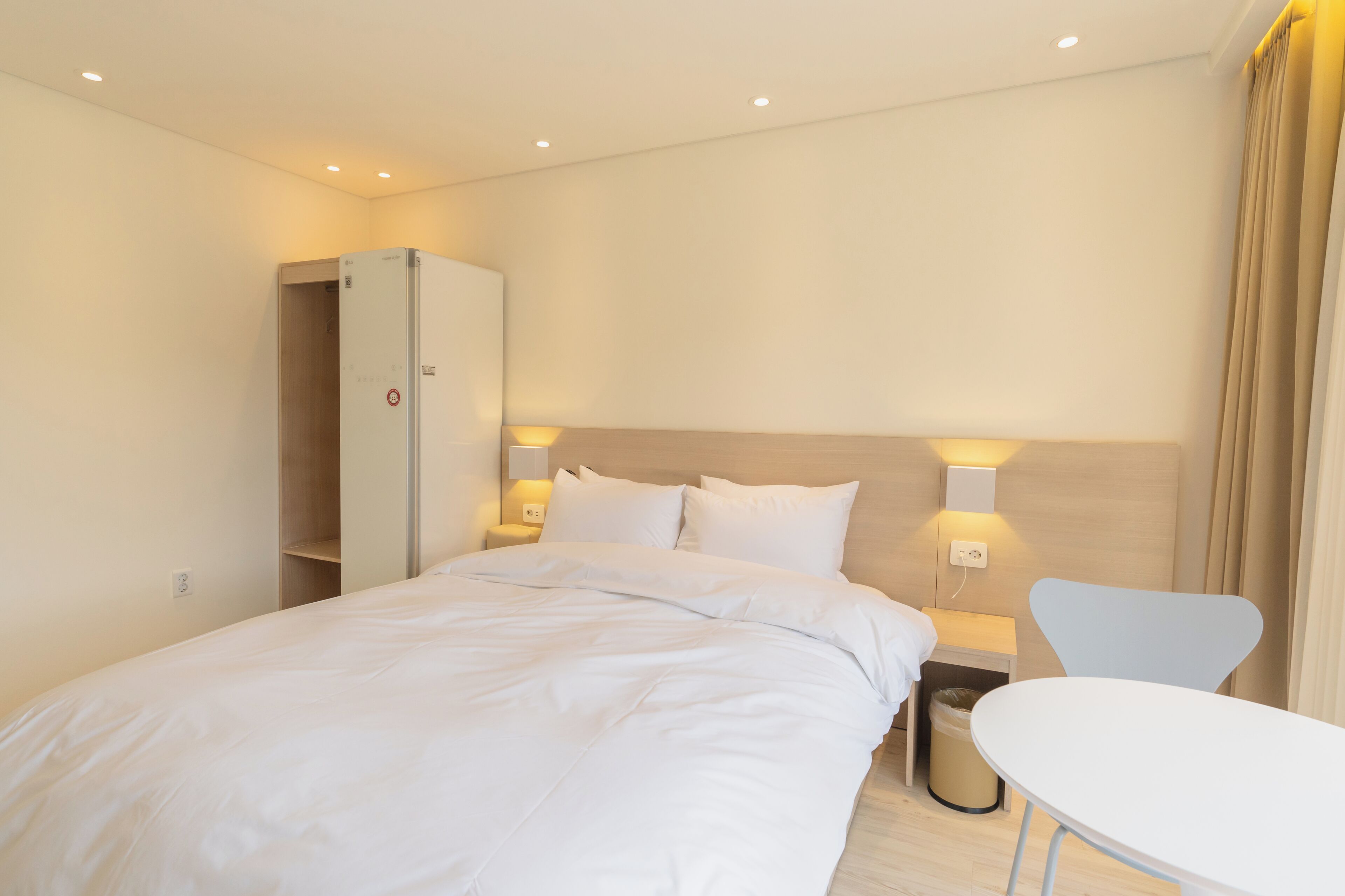 A hotel room with a bed, a wardrobe, a bedside table, and a chair.