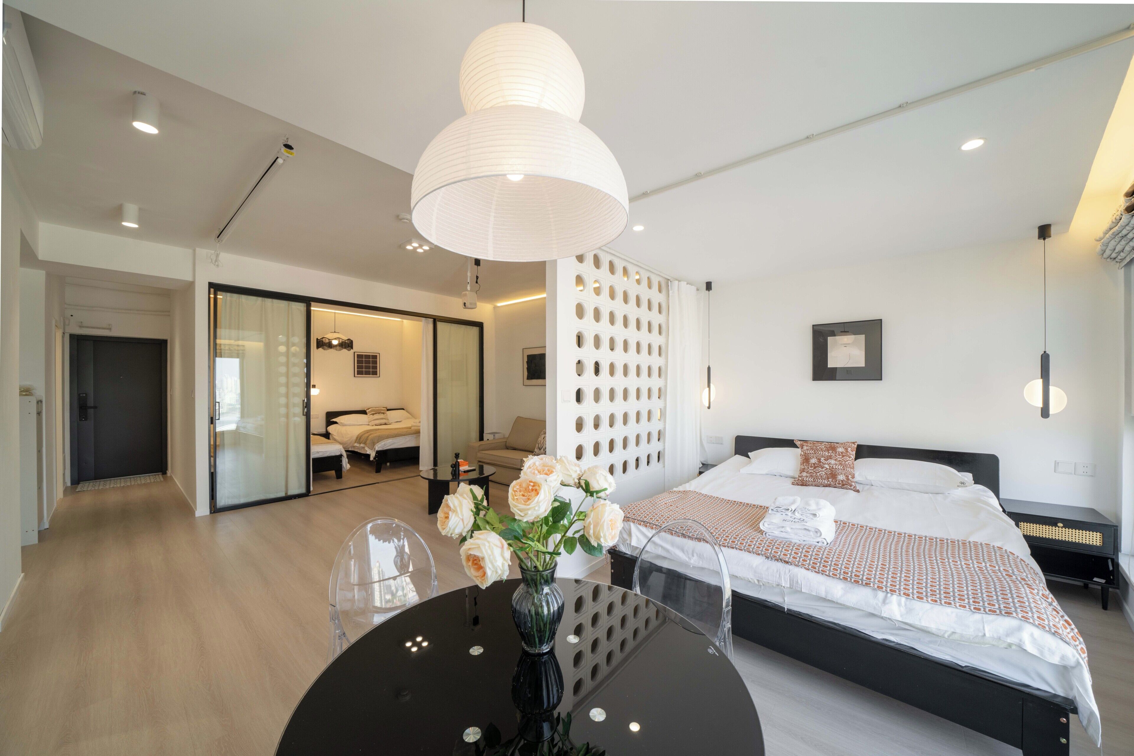 Een moderne hotelkamer met een groot bed, een eettafel met een bloevas, een apart zithoekje met een bank en fauteuils, en een glazen schuifdeur naar een balkon.