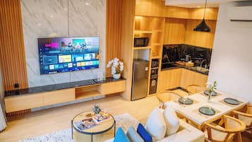 Una sala moderna con un televisor de pantalla plana, un sofá, una mesa de centro y un comedor con una mesa preparada para cuatro.