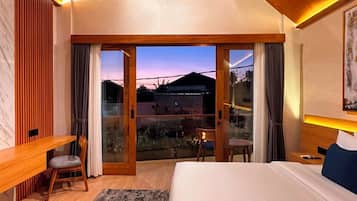 Un dormitorio con una cama grande, un escritorio y una silla. Hay una puerta corrediza de vidrio que da a un balcón.