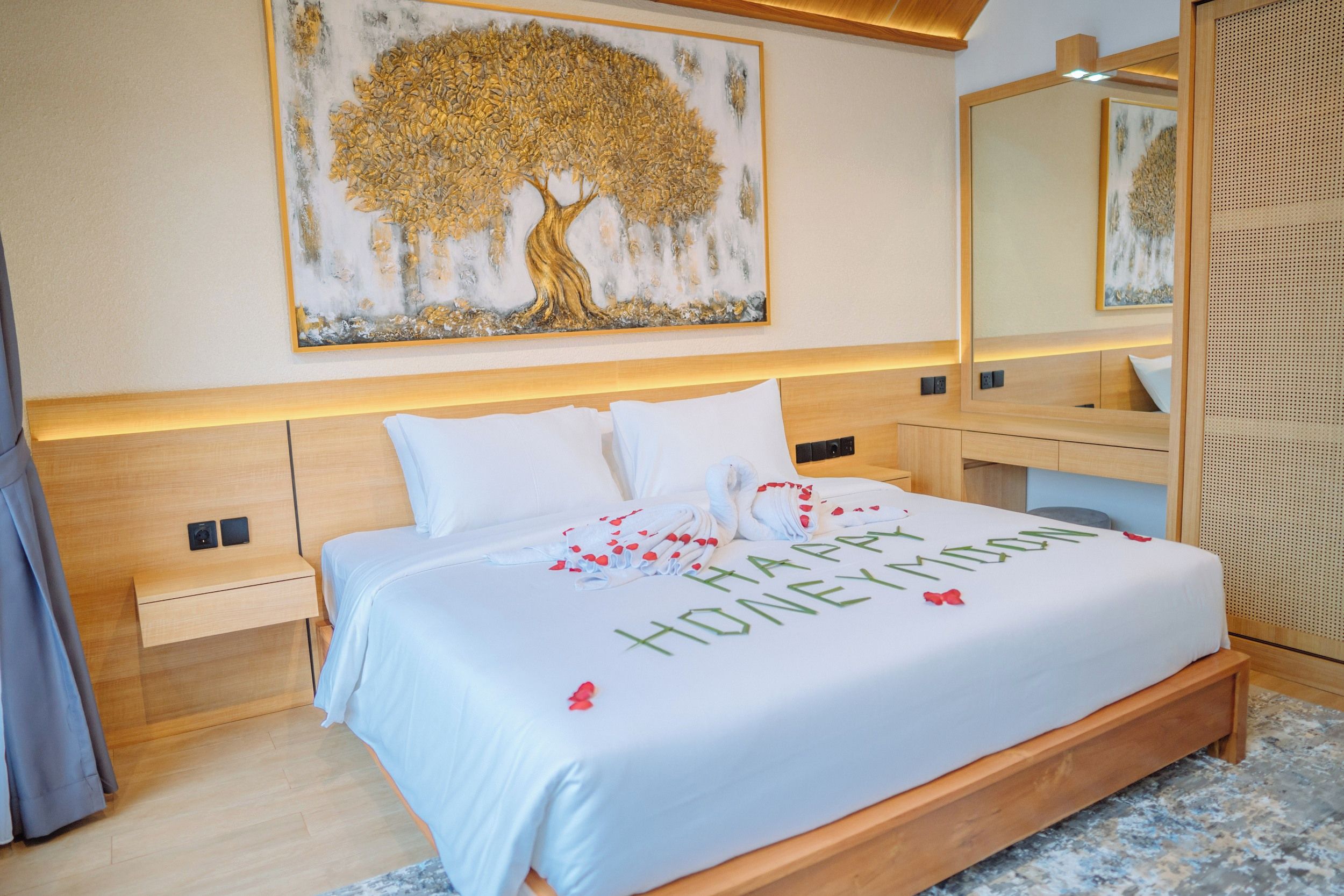 A hotel room with a large bed, a headboard, a bedside table, a nightstand, a mirror, and a wall-mounted artwork.