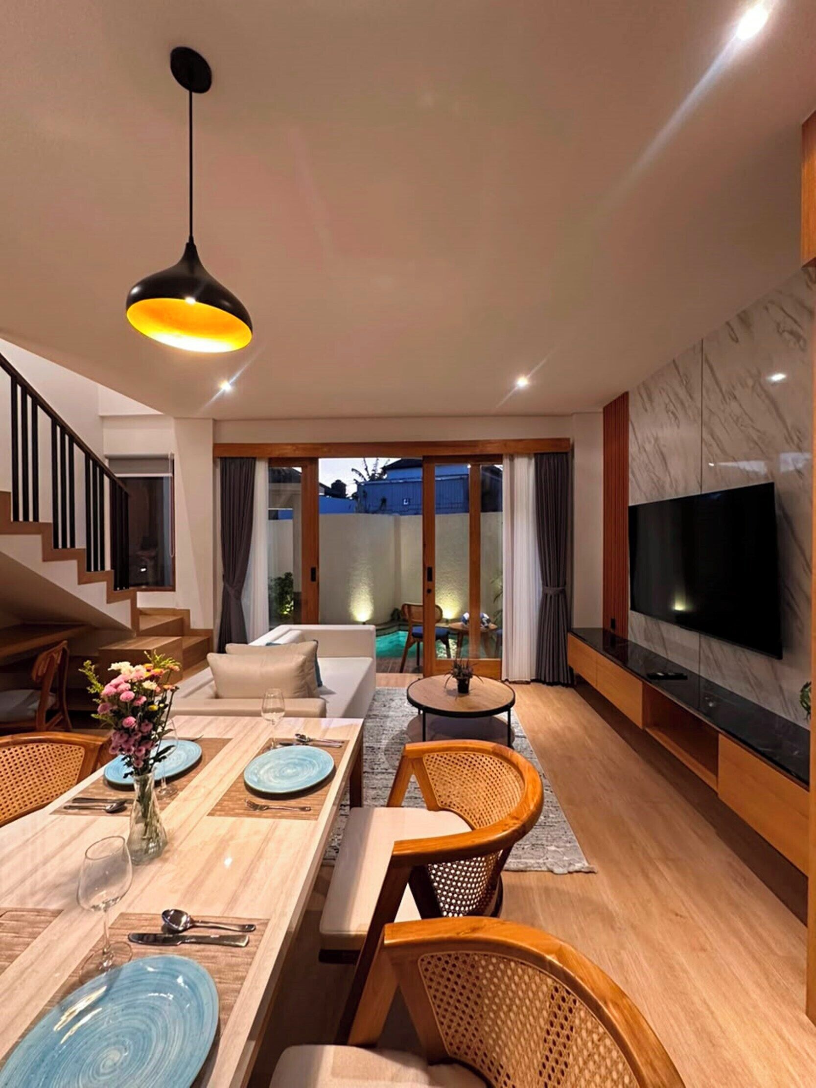 A modern living room with a dining area, a staircase, and a TV mounted on the wall.