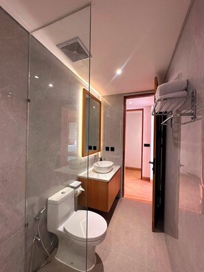 A modern bathroom with a glass-enclosed shower, a white toilet, a wooden vanity with a sink, and a mirror above the vanity. - Arkira Villas Ungasan (Indonesia)