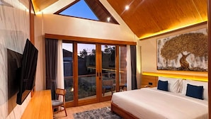 Un dormitorio con una cama grande, televisor, banca de madera y vistas al exterior a través de un ventanal.