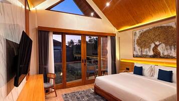 Ein Schlafzimmer mit einem großen Bett, einem Fernseher, einer Holzbank und Blick ins Freie durch eine Glastür.
