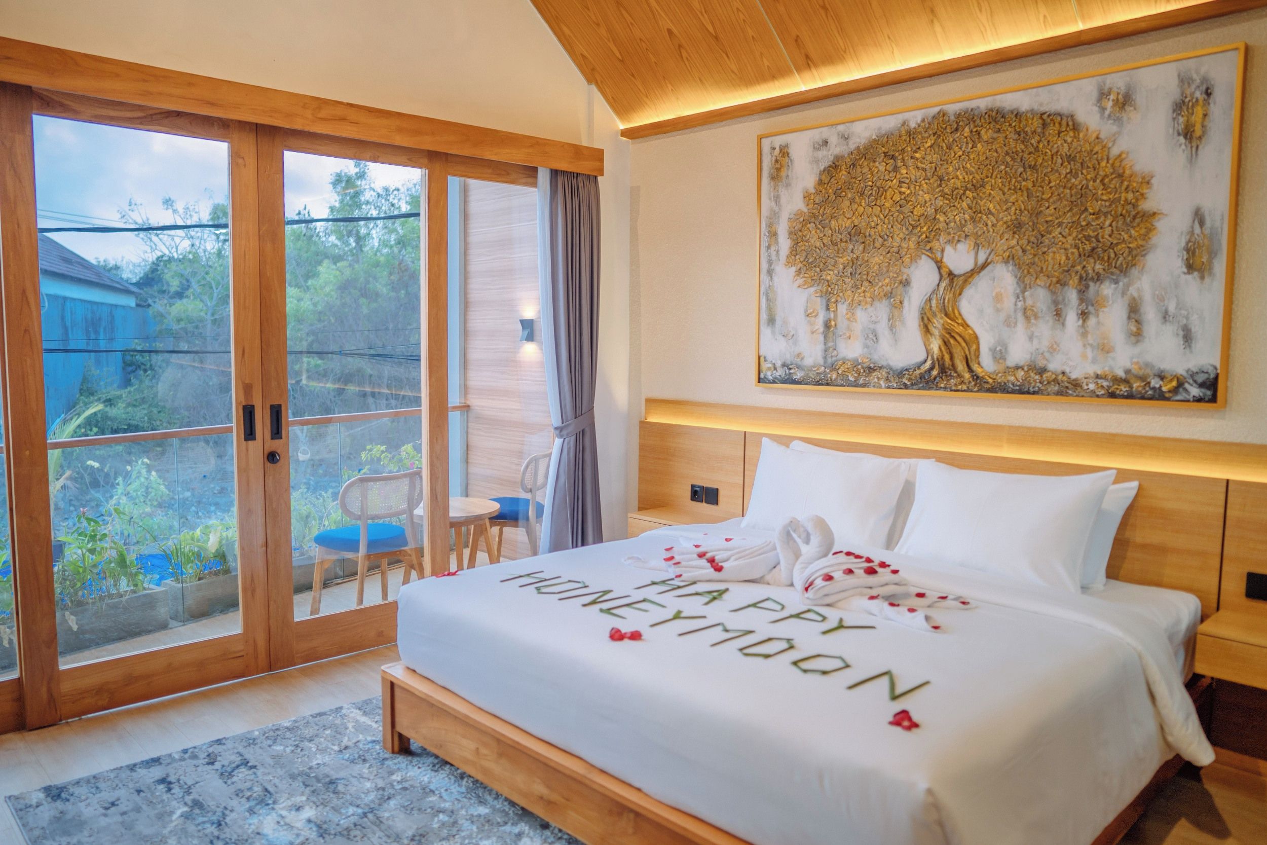 Une chambre d’hôtel avec un lit, un tableau représentant un arbre et une vue à travers les portes vitrées.