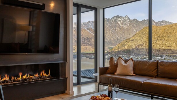Un salon moderne doté d’une cheminée, d’un canapé, d’un téléviseur et d’une grande fenêtre offrant une vue sur les montagnes.
