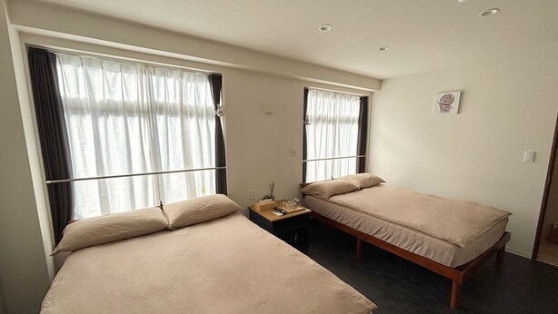 A room with two beds, a small table, and a window with curtains. - cozey retreat asakusabashi (Tokyo)