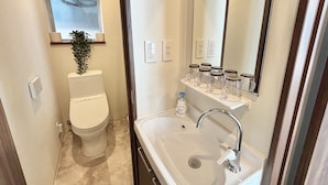 A bathroom with a toilet, sink, and a shelf with toiletries. - cozey retreat asakusabashi (Tokyo)