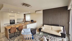 A modern living space with a kitchen, dining area, and a sofa by a large window. - Vacation rental 2 bedrooms, air conditioning, Wi-Fi, balcony, barbecue, private parking (ST MANDRIER SUR MER)