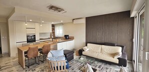 Ein modernes Wohnzimmer mit Küche, Essbereich und einer Couch neben einem großen Fenster.