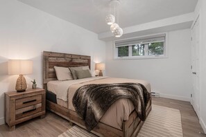 A bedroom with a wooden headboard, a large bed with a fur throw, bedside lamps, a nightstand, and a window with a view of trees.