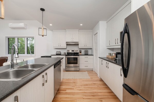 A modern kitchen with stainless steel appliances, white cabinetry, and a wooden floor.