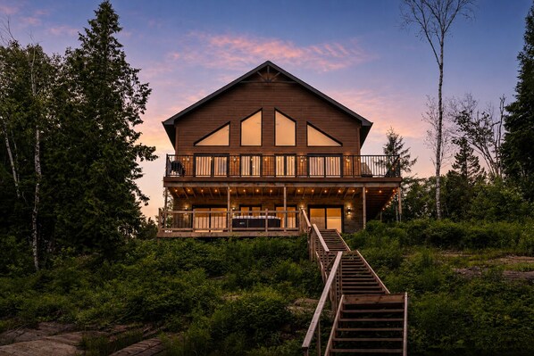 A two-story wooden cabin with a balcony, surrounded by dense greenery.
