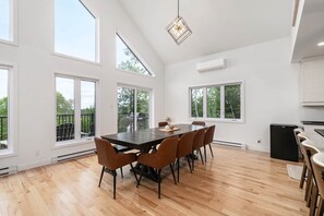 A spacious room with a large dining table, multiple chairs, and a modern pendant light.